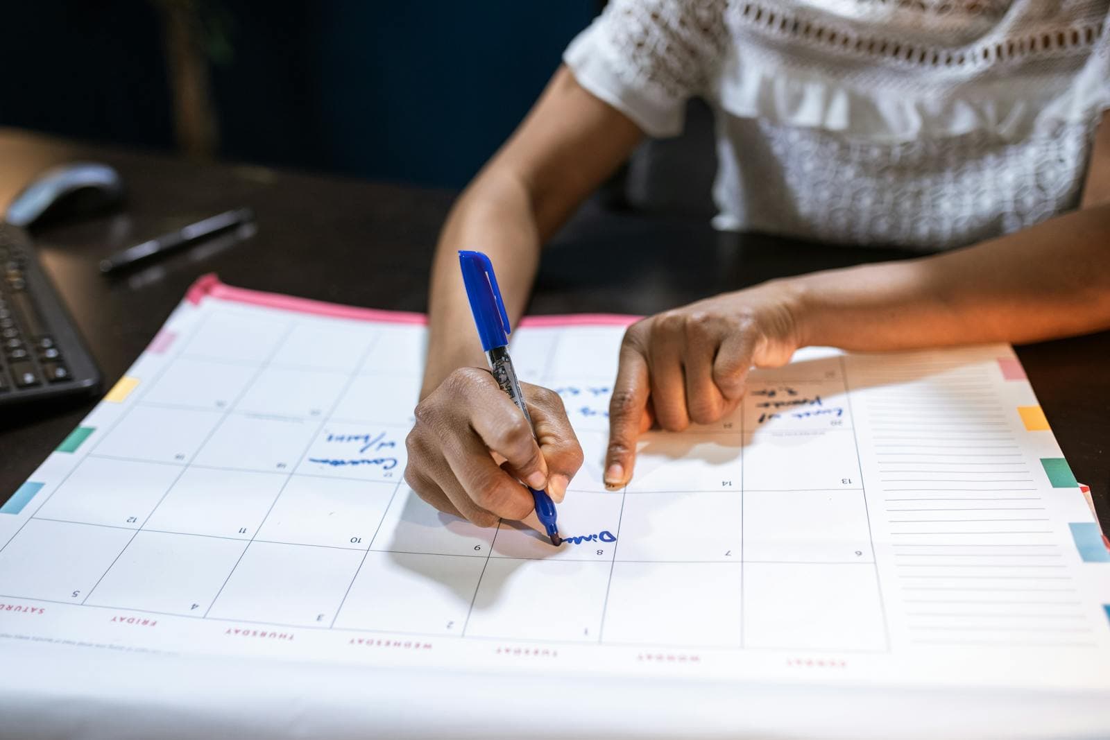 Person writing on a paper calendar while organizing date notes at a desk.