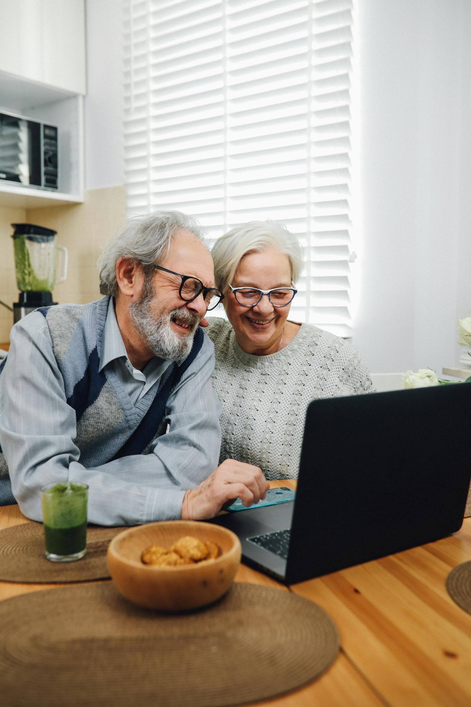 Senior couple smiling while using a laptop together at home.